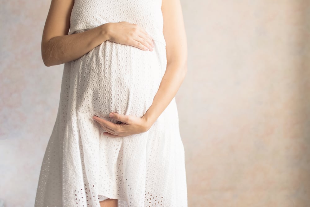 Pregnant woman in dress holds hand on belly